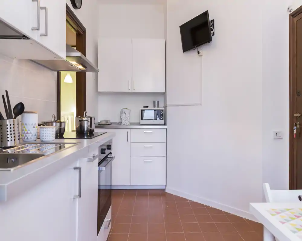 Bright, modern kitchenette with white cabinets, built-in oven, sink and countertop appliances; compact and tidy layout ideal for a small apartment.
