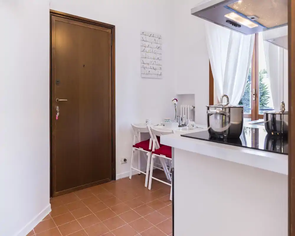 Small entrance area opening directly into a compact kitchen/dining corner; wooden front door, tiled floor and a countertop with cooking pots visible.