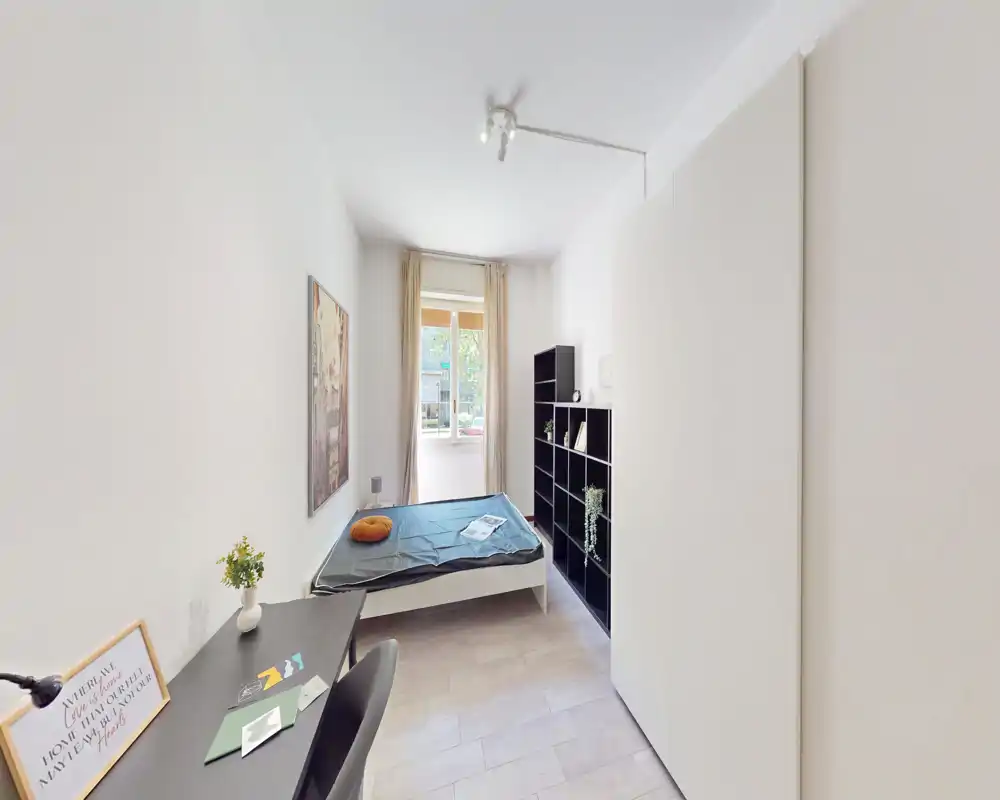 Camera da letto luminosa e compatta con letto singolo vicino alla finestra, scrivania, libreria e armadio — stile moderno e luce naturale.