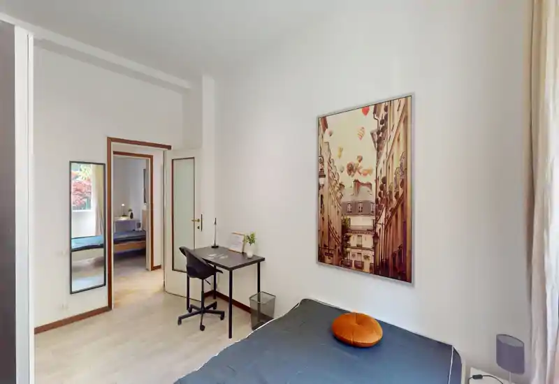 Camera da letto moderna e luminosa con letto singolo, scrivania e quadro decorativo. Pavimento chiaro e angolo studio ben illuminato dalla finestra.