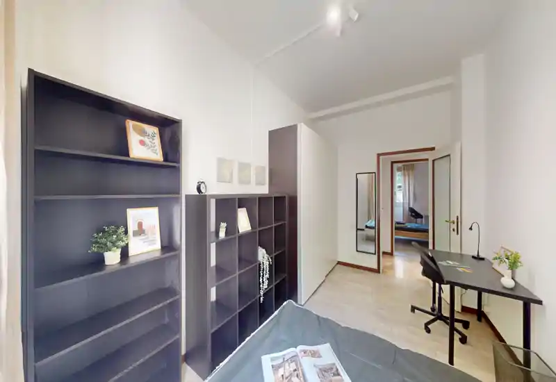 Camera da letto singola luminosa e moderna con letto in primo piano, grandi scaffali, scrivania e uno specchio vicino alla porta — ben illuminata e arredata con cura per un annuncio.