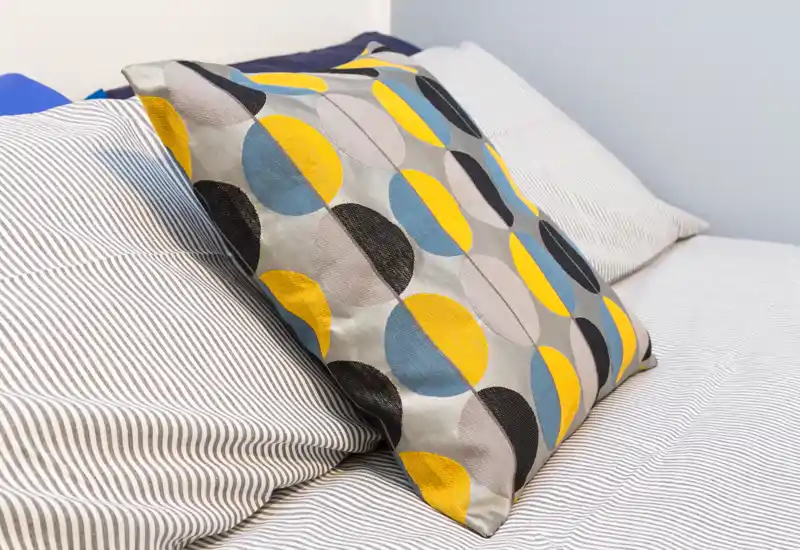 Plano detalle de una cama bien hecha con cojín decorativo estampado, ropa de cama a rayas y almohadas suaves — ideal para mostrar el estilo del dormitorio.