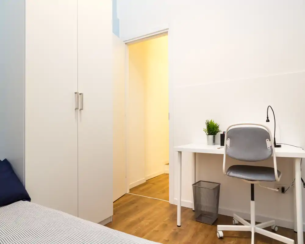 Camera compatta con letto singolo, armadio a muro e una piccola scrivania con sedia; luminosa, pulita e dallo stile minimale, adatta per soggiorni brevi.