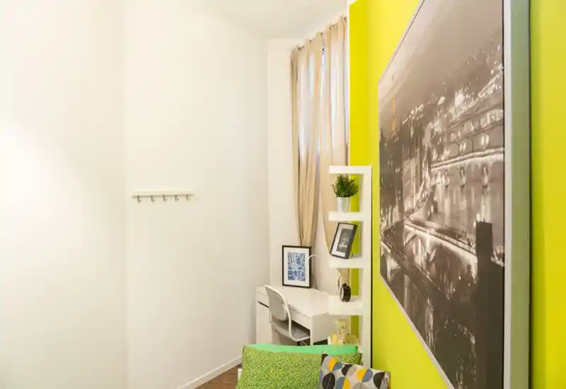 Small, stylish living corner with a bright green accent wall, a comfortable cushion area and a compact desk with shelving — ideal for a cozy studio or a workspace within the living area.