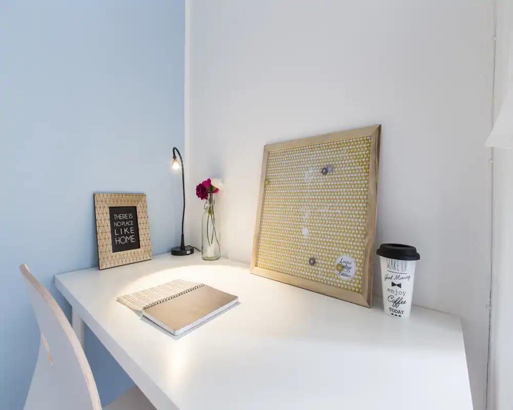 Coin bureau lumineux et minimaliste avec plateau blanc, petite lampe, carnet, cadres décoratifs et gobelet de café — parfait pour un espace de travail.