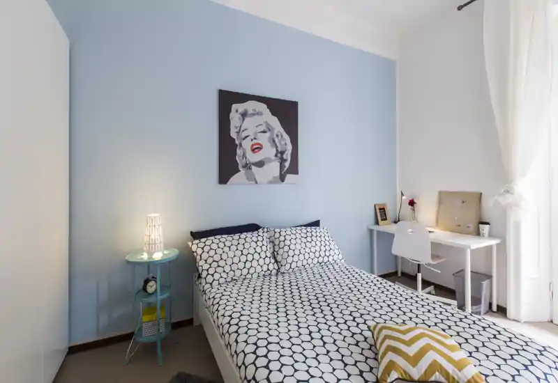 Dormitorio luminoso y con estilo, con cama doble y ropa de cama geométrica, lámpara de noche y un pequeño escritorio junto a la ventana — perfecto para descansar y trabajar a la vez.