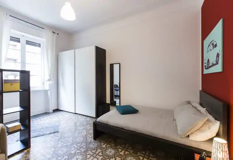 Chambre lumineuse et soignée avec un lit double confortable, une armoire et un mur d'accent décoratif; carrelage à motifs et grande fenêtre offrent une ambiance accueillante.