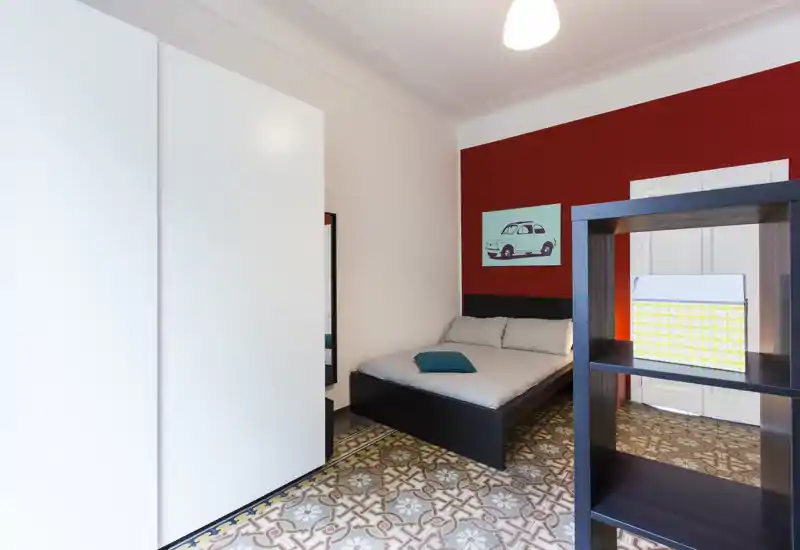 Chambre soignée avec lit double contre un mur d'accent rouge, œuvre décorative et carrelage à motifs ; bien éclairée et agencée pour les locations courte durée.