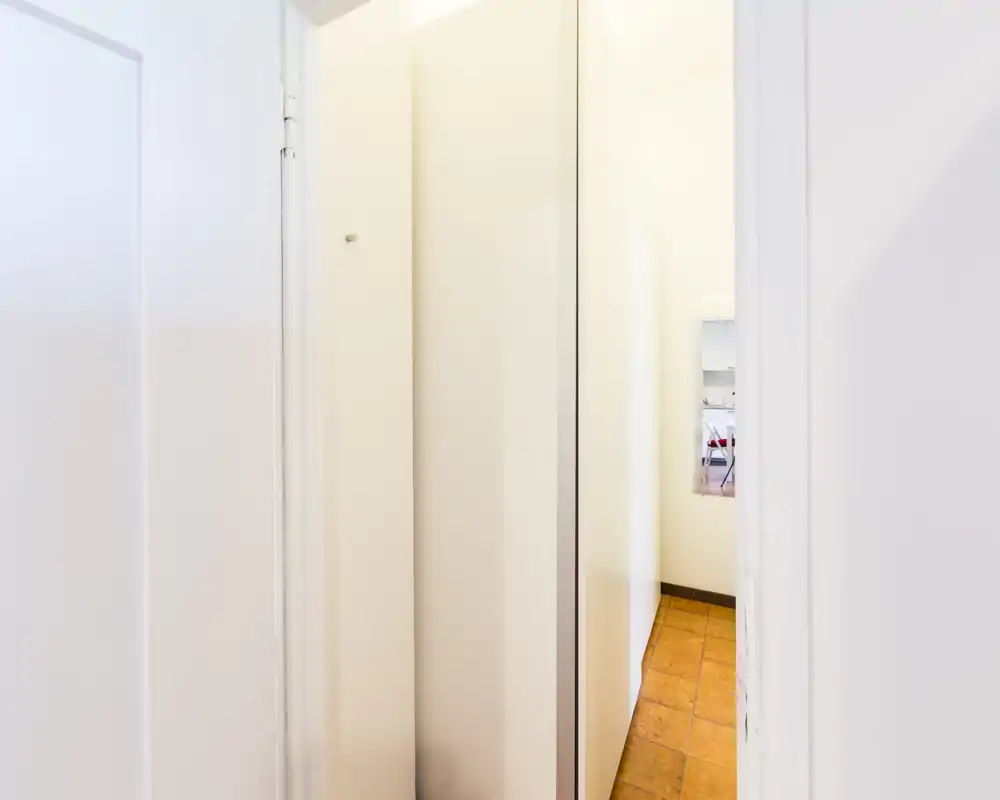 Entrada/pasillo estrecho con paredes blancas y suelo de baldosas; pasillo luminoso y minimalista que conduce al piso.