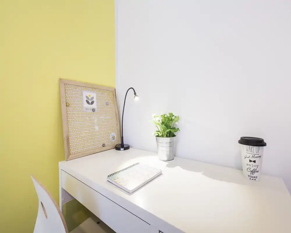 Espacio de trabajo luminoso y minimalista con escritorio blanco, lámpara, una pequeña planta en maceta y un corcho — ideal para estudiar o trabajar concentrado.