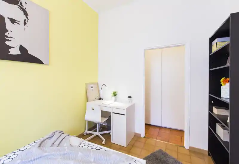 Dormitorio luminoso y ordenado con rincón de cama acogedor, escritorio blanco compacto y estantería — ideal para estudiante o persona sola.