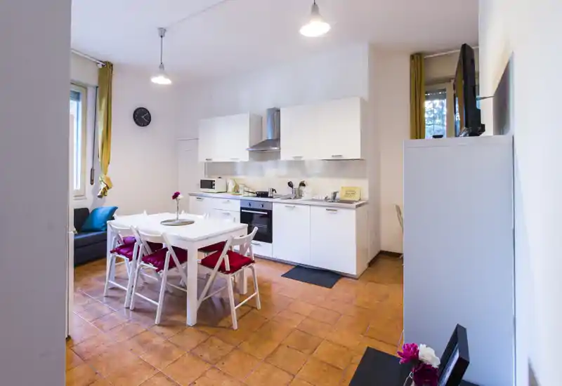 Cocina abierta moderna y luminosa con armarios blancos y mesa central para cuatro; suelos de terracota y detalles alegres crean un espacio acogedor ideal para alquileres vacacionales.