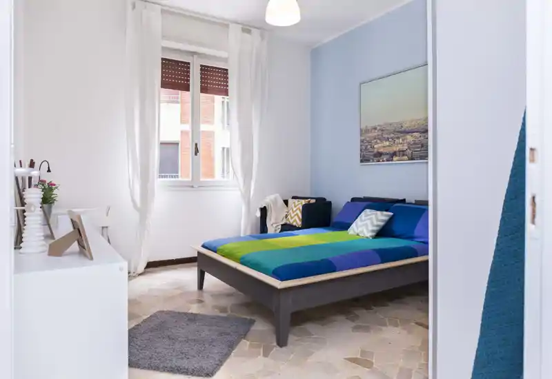 Camera da letto luminosa e ben arredata con letto matrimoniale dai colori vivaci, luce naturale da una grande finestra e decorazioni semplici ed eleganti.