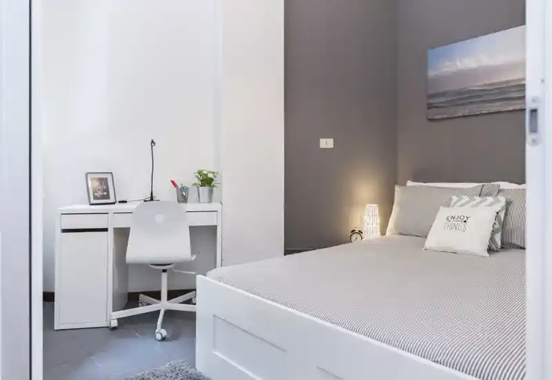 Dormitorio moderno y luminoso con una cama doble cómoda, cojines decorativos y un pequeño escritorio blanco ideal para trabajar o estudiar.