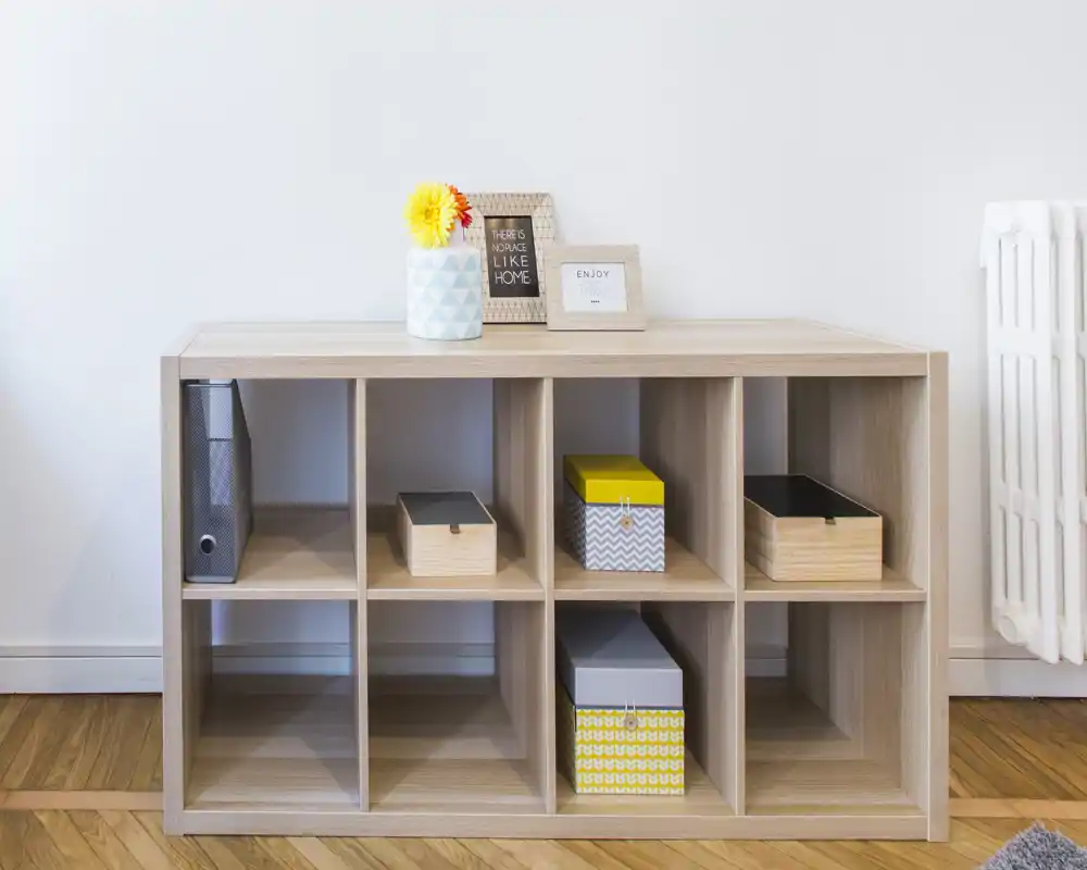 A bright, minimal living-area shot focusing on a wooden cubed shelving unit with decorative boxes, a vase and framed signs—ideal for showcasing storage and styling in a living room.
