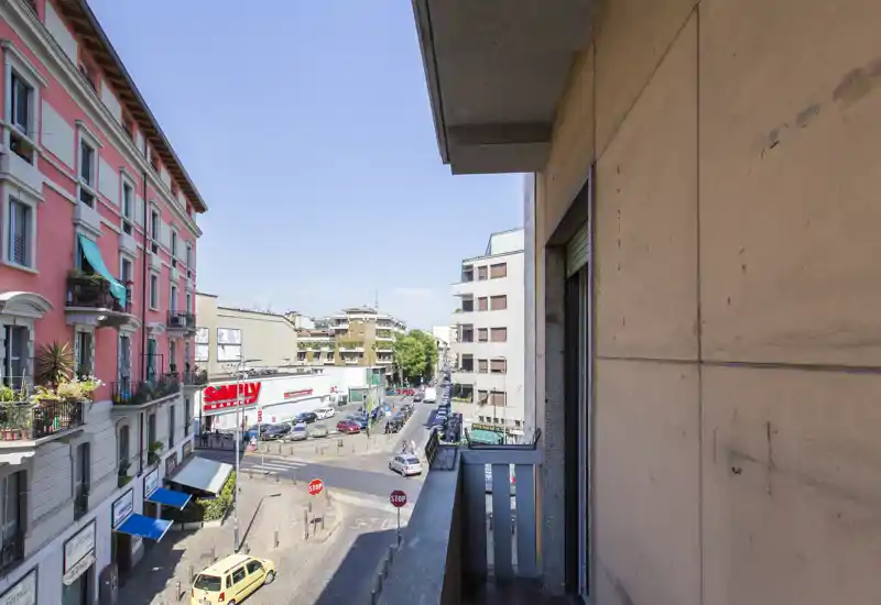Petit balcon ensoleillé donnant sur une rue animée de la ville, avec vue sur les immeubles et commerces voisins.