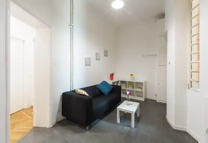 Petit séjour bien aménagé avec canapé noir, coussins, table basse et étagères — lumineux et soigné, parfait pour une location en ville.