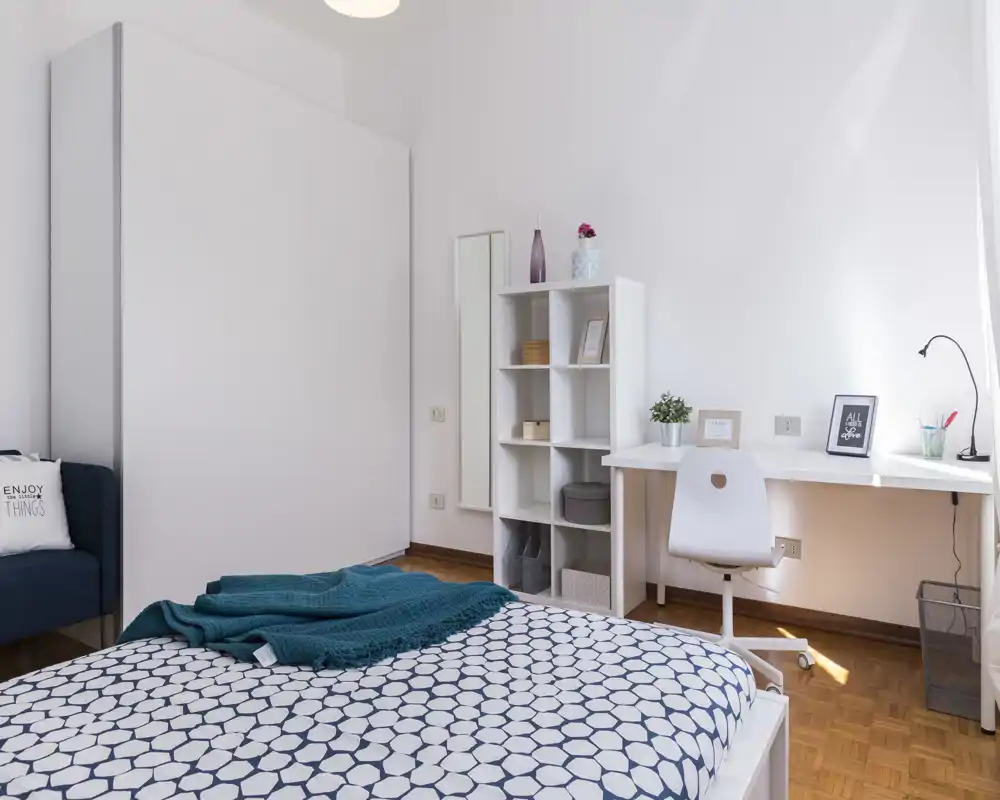 Dormitorio moderno y luminoso con colcha estampada, manta turquesa y escritorio blanco junto a la ventana — ordenado y minimalista.