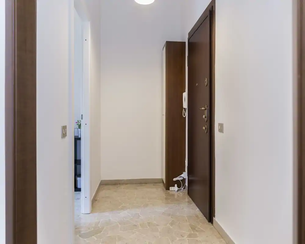 Recibidor luminoso y minimalista con puerta de entrada de madera, portero eléctrico y mueble estrecho — suelo de mármol y paredes neutras que transmiten orden.