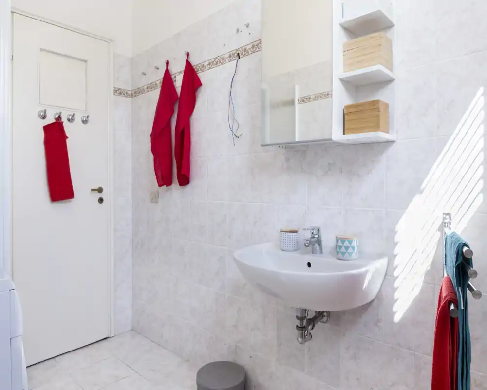 Baño limpio y bien iluminado con lavabo suspendido, mueble con espejo y paredes alicatadas; toallas de colores aportan contraste.
