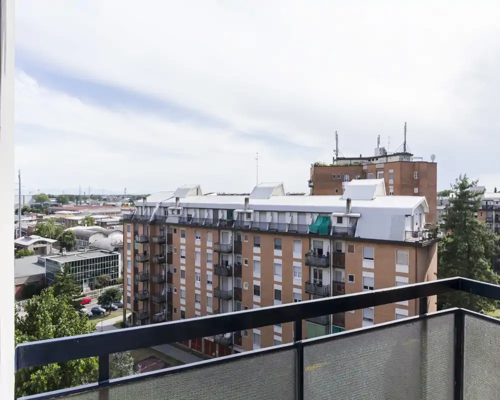 Balcón privado soleado con barandilla metálica y vistas a edificios de ladrillo y copas de árboles — ideal para el café de la mañana o relajarse al aire libre.