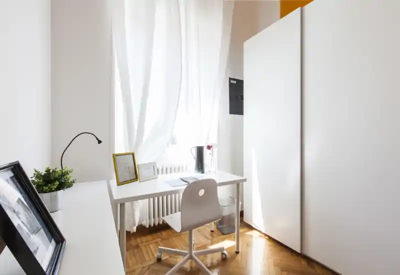 Coin bureau lumineux et minimaliste avec bureau blanc, chaise pivotante et grande fenêtre avec voilages, offrant une lumière naturelle et un espace de travail propre et fonctionnel.