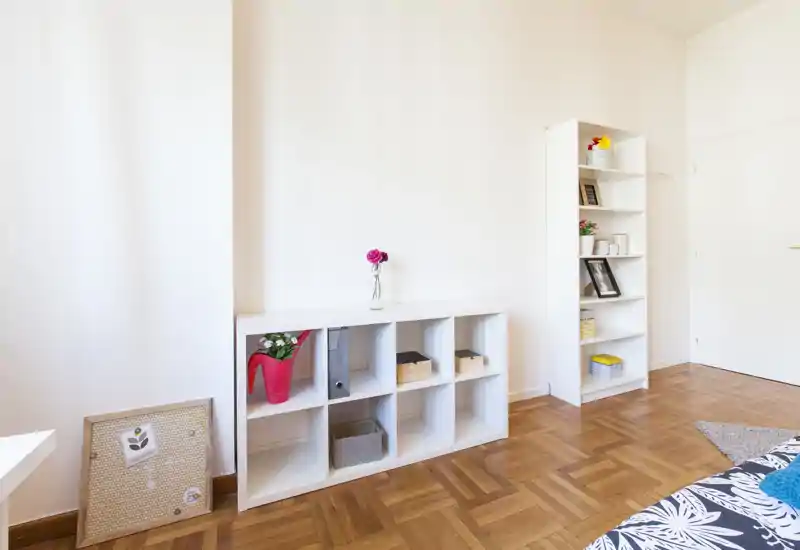 Coin de chambre minimaliste et lumineux avec une partie du matelas visible, étagères blanches et parquet; décoration simple et lumière naturelle pour une ambiance épurée.