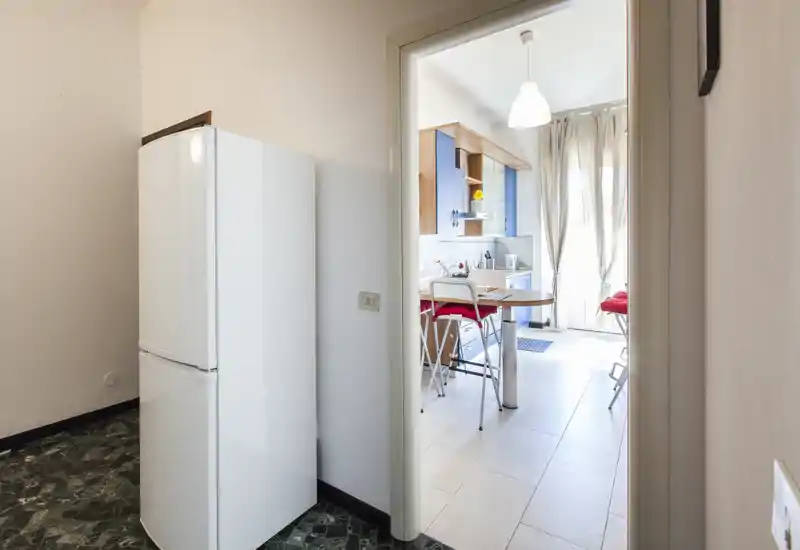 Cuisine compacte et lumineuse visible à travers une porte : meubles en bois, petite table avec tabourets et lumière naturelle – pratique et conviviale pour les courts séjours.