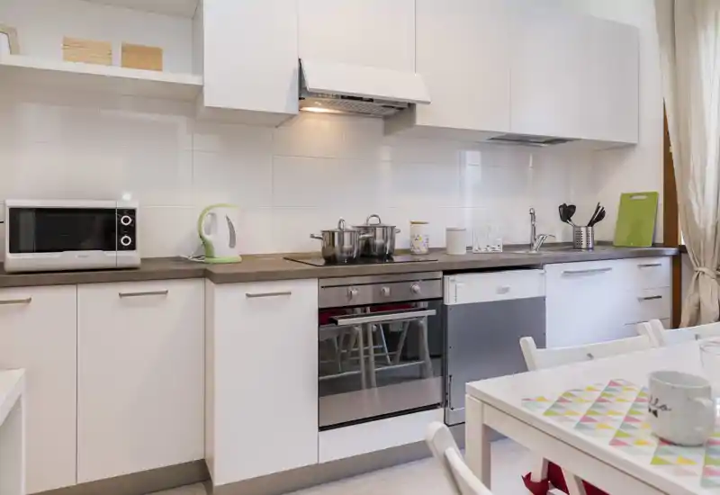 Bright modern kitchen with white cabinetry, built-in oven, dishwasher and a small dining table — clean, functional space ideal for short-term stays.