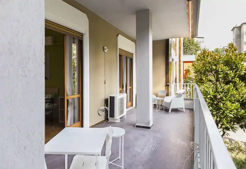 Sunny furnished balcony with outdoor seating and table, connected to interior through sliding doors — ideal for morning coffee.