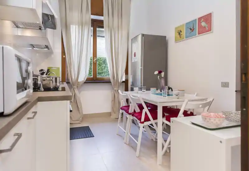 Bright, tidy kitchen with a small dining table for four, white cabinets, and a window providing natural light—ideal for cozy meals.