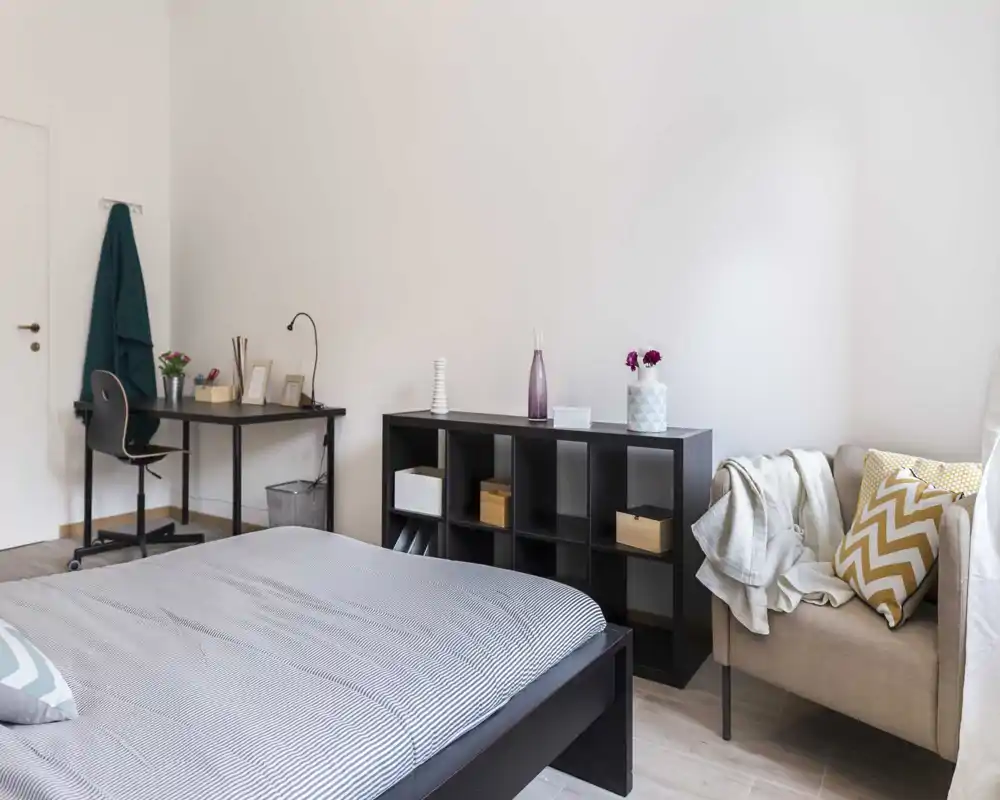 Camera da letto moderna e luminosa con letto ben rifatto, scrivania compatta e libreria a cubi; toni neutri e tessuti morbidi creano un'atmosfera calma e accogliente.