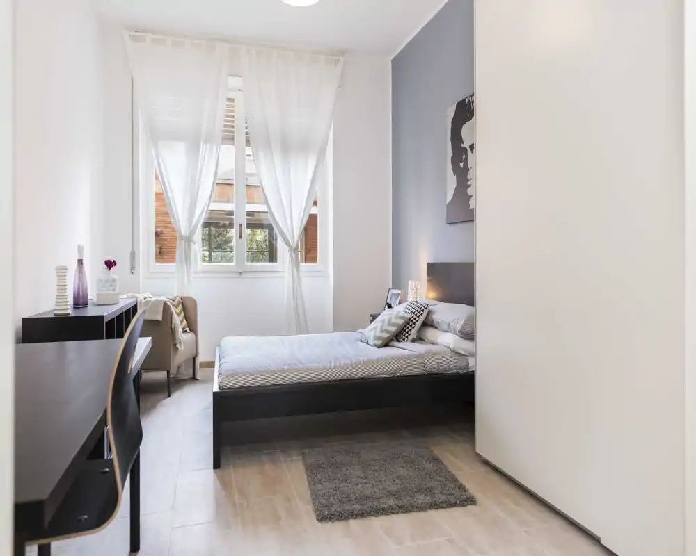 Camera da letto moderna e luminosa con letto matrimoniale, tessili morbidi e una grande finestra che offre molta luce naturale.