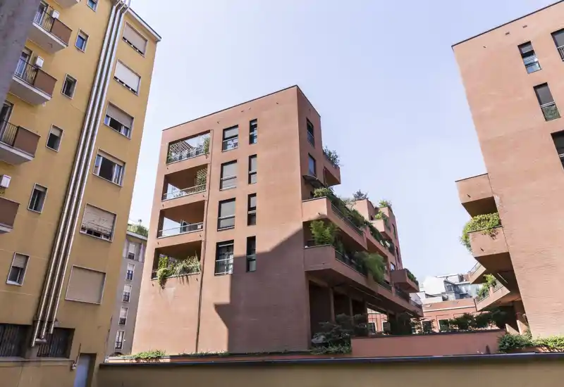 Vue extérieure d'une cour résidentielle avec des immeubles en brique modernes, des terrasses et de la végétation sous une lumière claire — parfait pour mettre en valeur la façade et les espaces extérieurs.