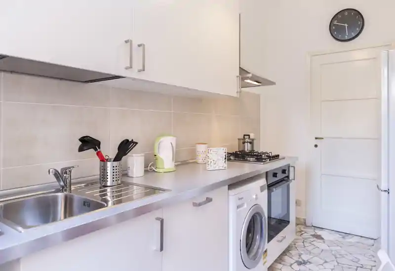 Cuisine moderne et lumineuse avec évier inox, four encastré et plaque à gaz, lave-linge sous le plan de travail et accessoires soignés.