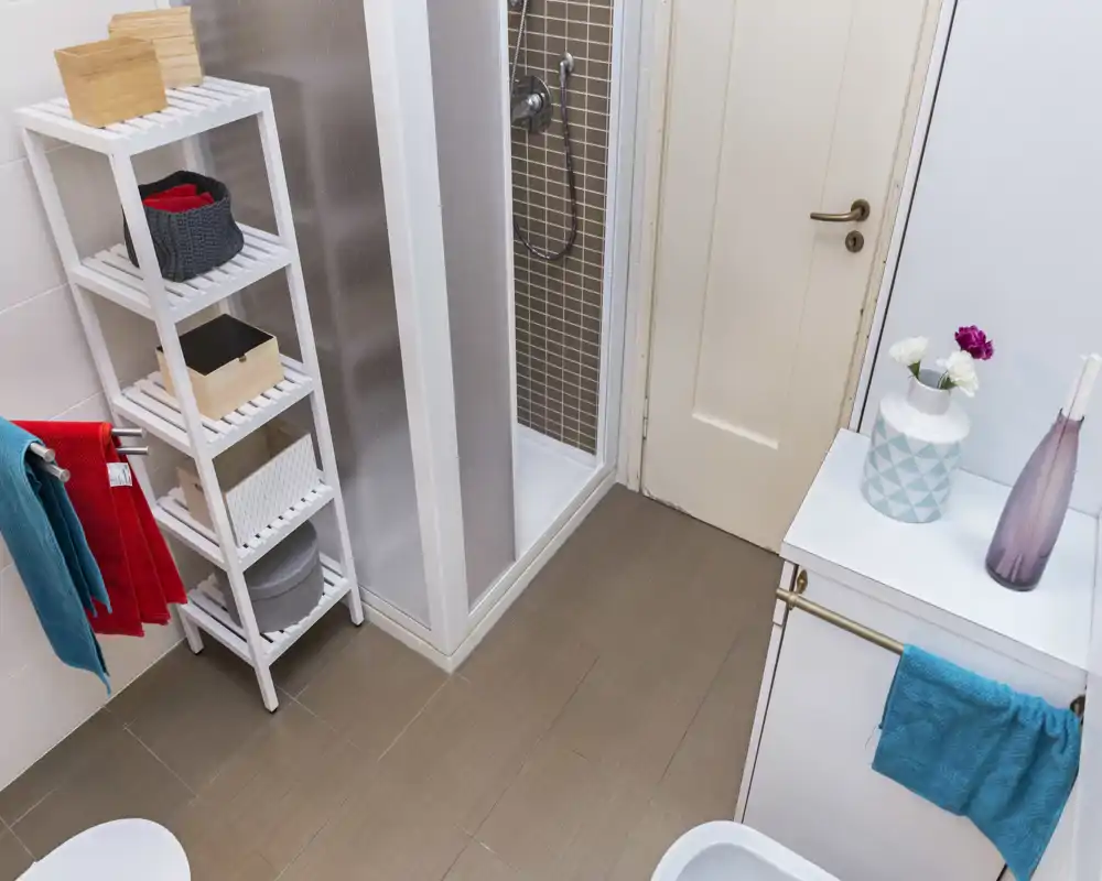Baño moderno y limpio con plato de ducha, toalleros y estantería; azulejos claros y accesorios ordenados que brindan un espacio funcional y luminoso.