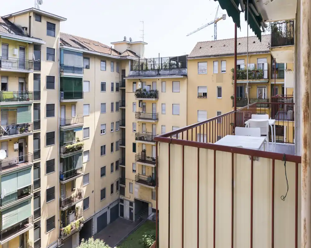 Balcón soleado del apartamento con vistas al patio interior y a los edificios vecinos; mesa y sillas para disfrutar al aire libre.