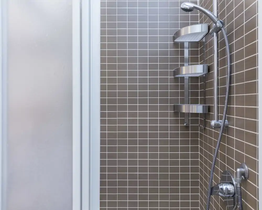 Ducha moderna con azulejos marrones, ducha de mano y estantes metálicos en la esquina — luminosa y lista para usar.