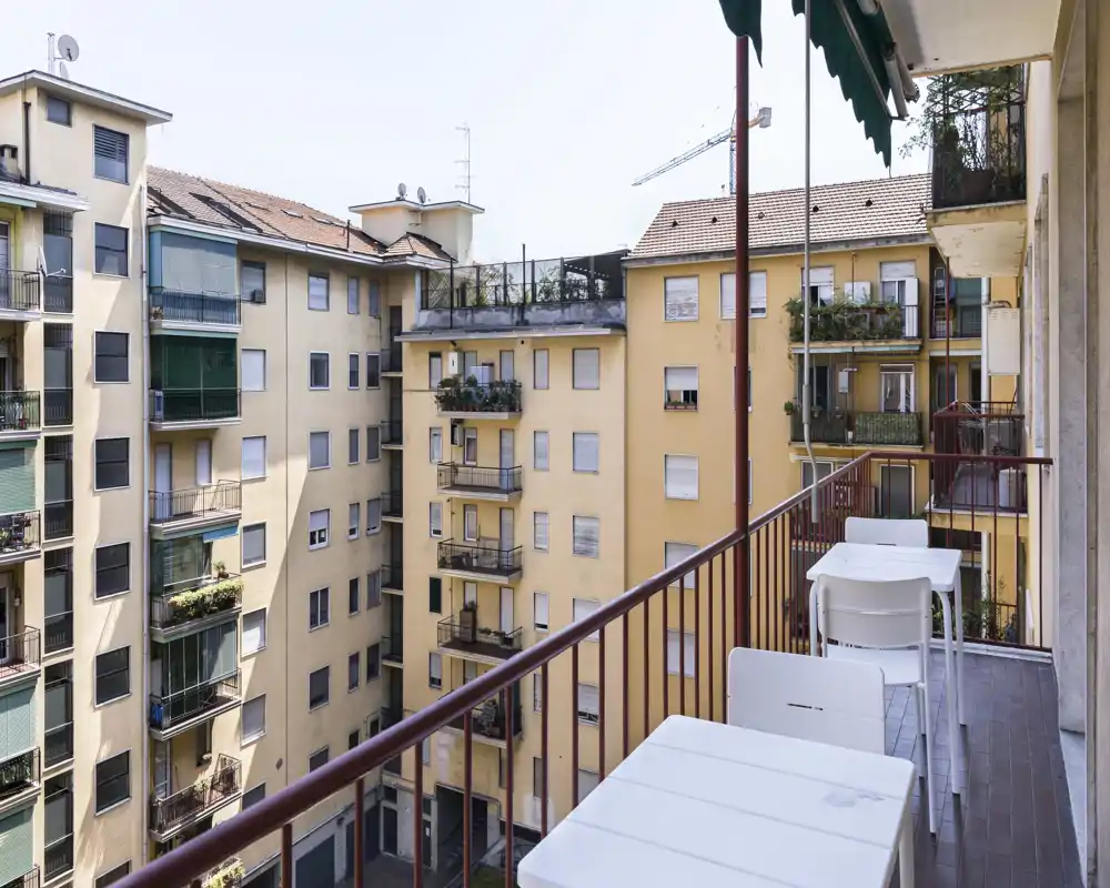 Balcón urbano soleado con dos pequeñas mesas y sillas, con vistas a edificios residenciales vecinos — ideal para tomar un café por la mañana o relajarse al aire libre.
