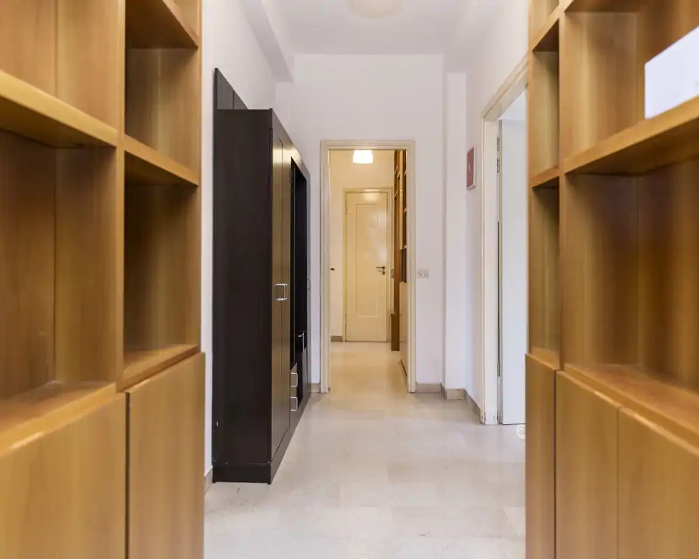 Entrada luminosa con estanterías empotradas de madera y vista clara hacia una puerta interior, ideal para almacenamiento y recibir invitados.