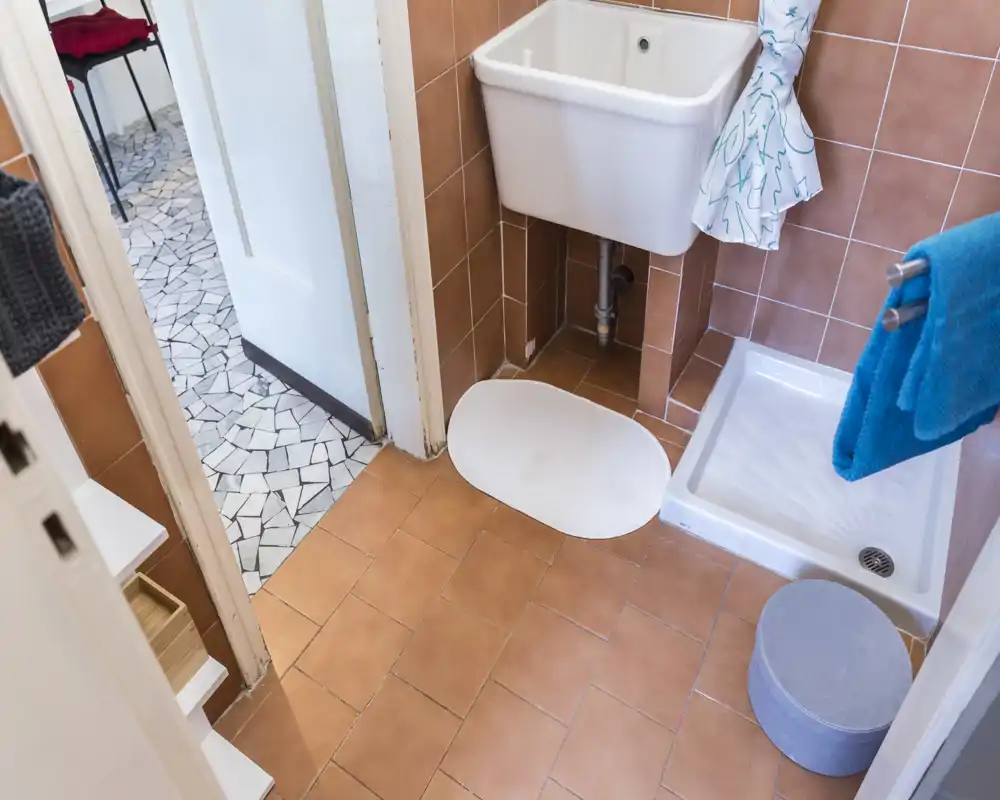 Baño compacto con plato de ducha, lavabo de pared y suelo de baldosas; espacio luminoso y funcional ideal para un piso pequeño.