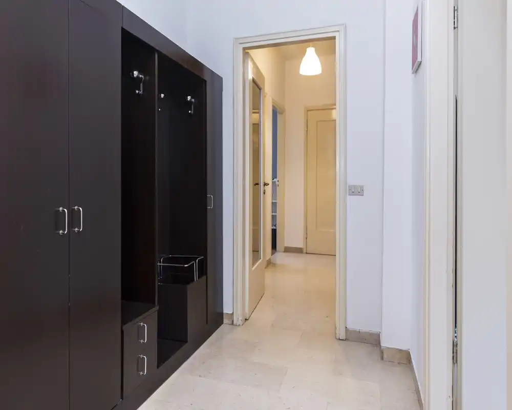 Entrada/pasillo luminoso con armario empotrado oscuro y suelo de baldosas, ideal para guardar abrigos y calzado.