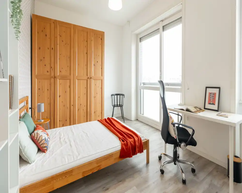 Bright, cozy bedroom with a wooden bed, wardrobe and a desk by a large window — ideal for working and relaxing.
