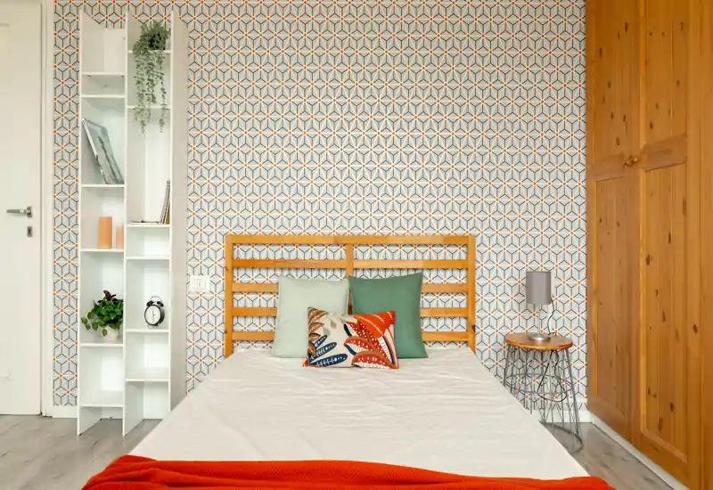 Bright, styled bedroom with a wooden headboard, patterned wallpaper and decorative cushions — cozy and ready for guests.