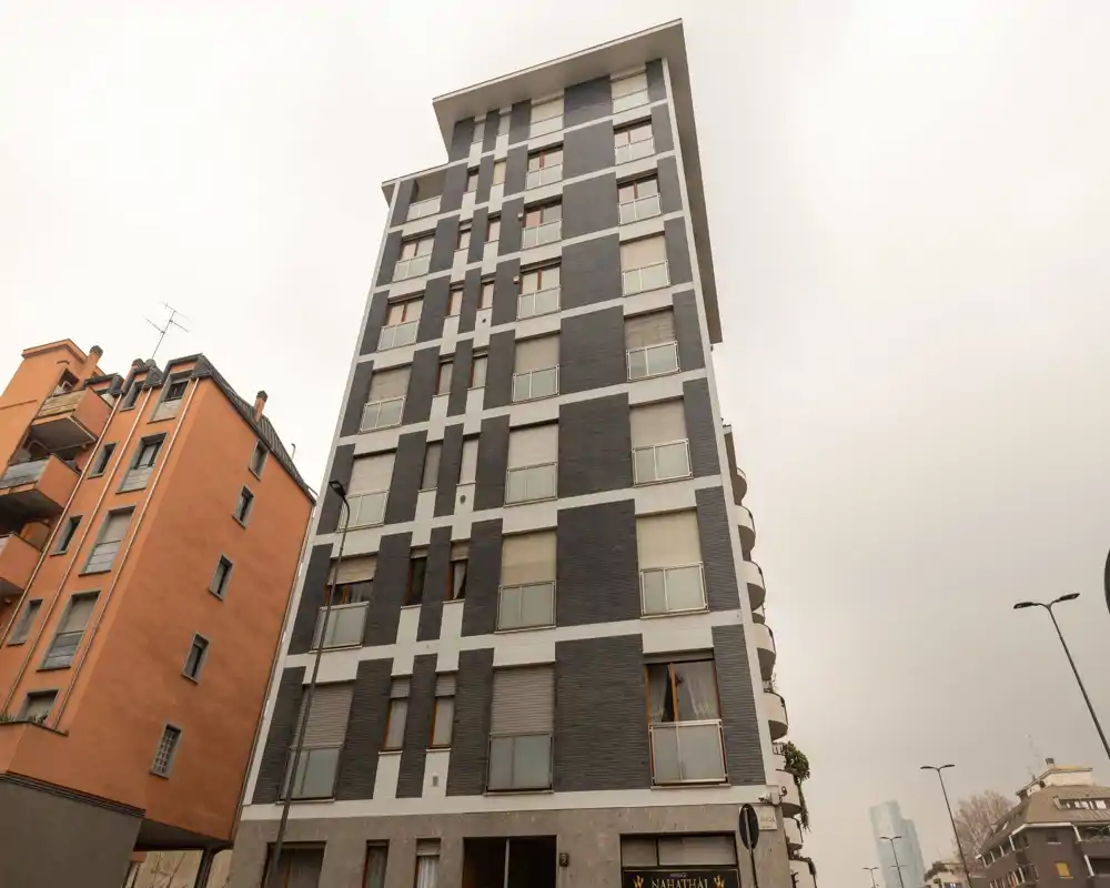 Exterior view of a modern multi-story residential building with grey and white façade and adjacent orange building; suitable photo to show the building’s exterior and street context.