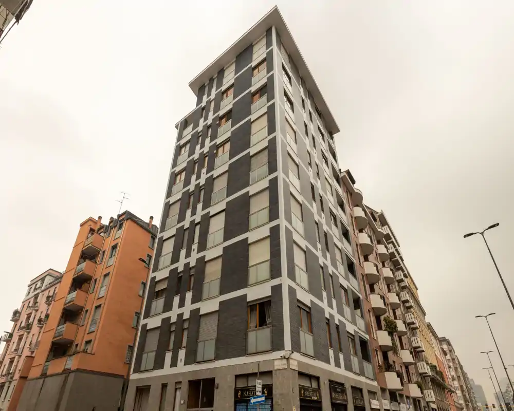 Exterior street view of a multi-story apartment building with modern gray-and-white facade and neighboring buildings; suitable for listing the building or facade but does not show any interior room.