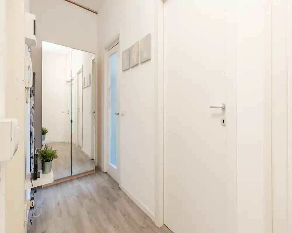 Bright, modern entrance hallway with light wood-effect floors, white doors and a full-height mirrored wardrobe that visually enlarges the space.