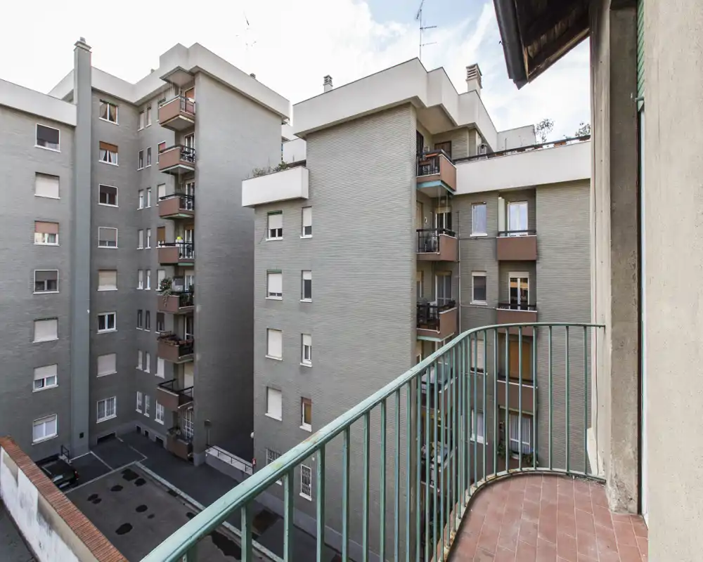 Piccolo balcone privato con vista sul cortile interno e sugli edifici circostanti; pavimento piastrellato e ringhiera in metallo offrono un angolo esterno pratico per un caffè mattutino.