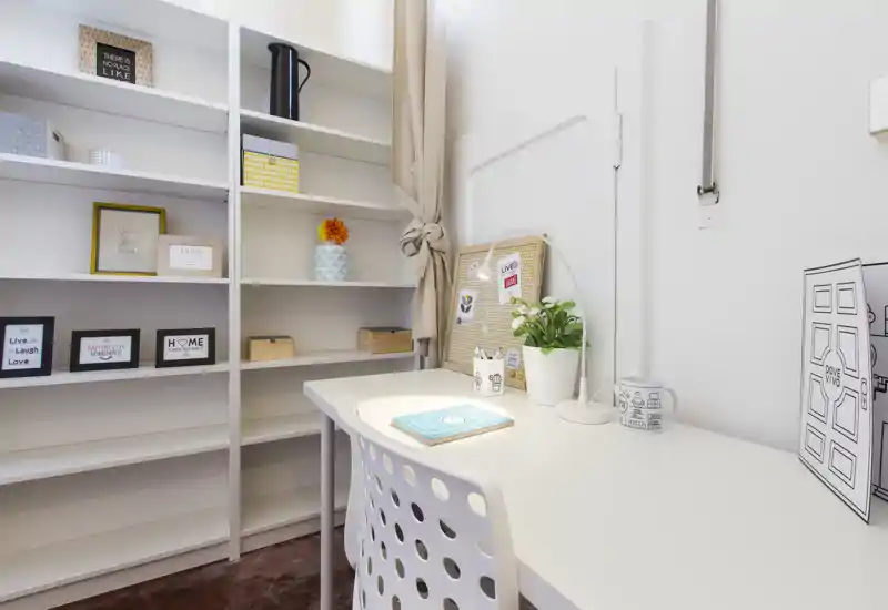 Angolo studio luminoso e ordinato con scrivania bianca, sedia e scaffalatura organizzata — ideale per smart working o lettura.