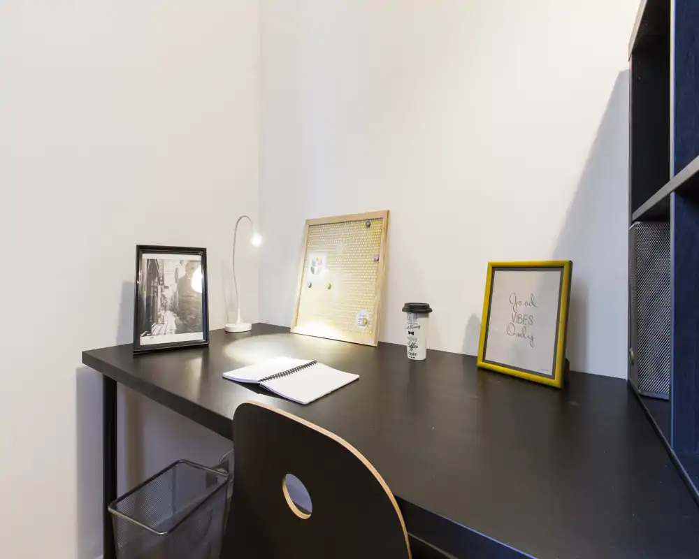 Zona studio ordinata con scrivania nera, lampada da lavoro, stampe incorniciate e bacheca: ideale per lavorare o leggere con concentrazione.